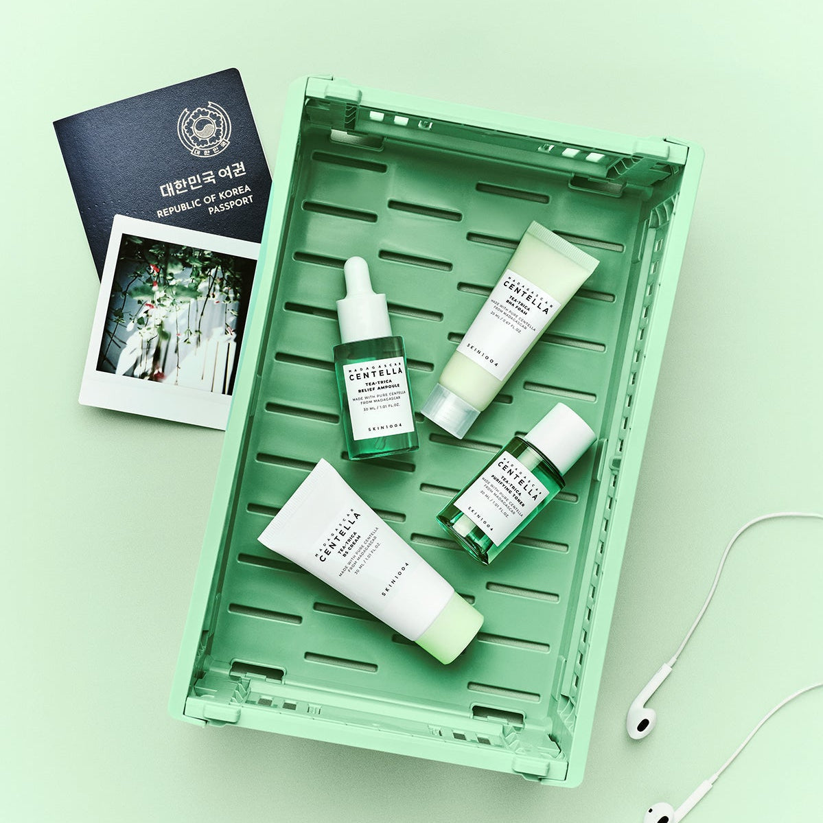 SKIN1004 Madagascar Centella Teatrica Travel Kit displayed in a tray with travel essentials including a passport and headphones.