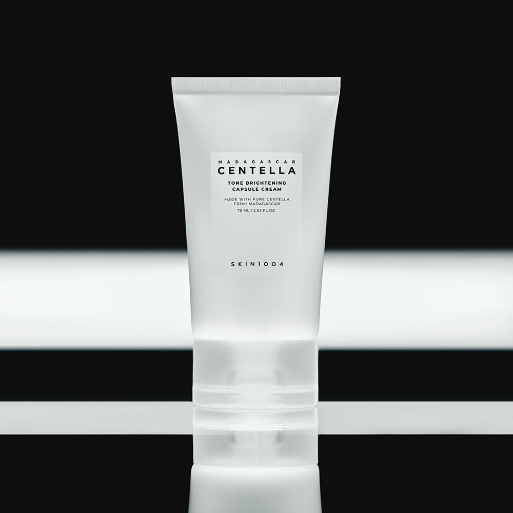 SKIN1004 Madagascar Centella Tone Brightening Capsule Cream 75ml in a sleek tube on reflective black surface.