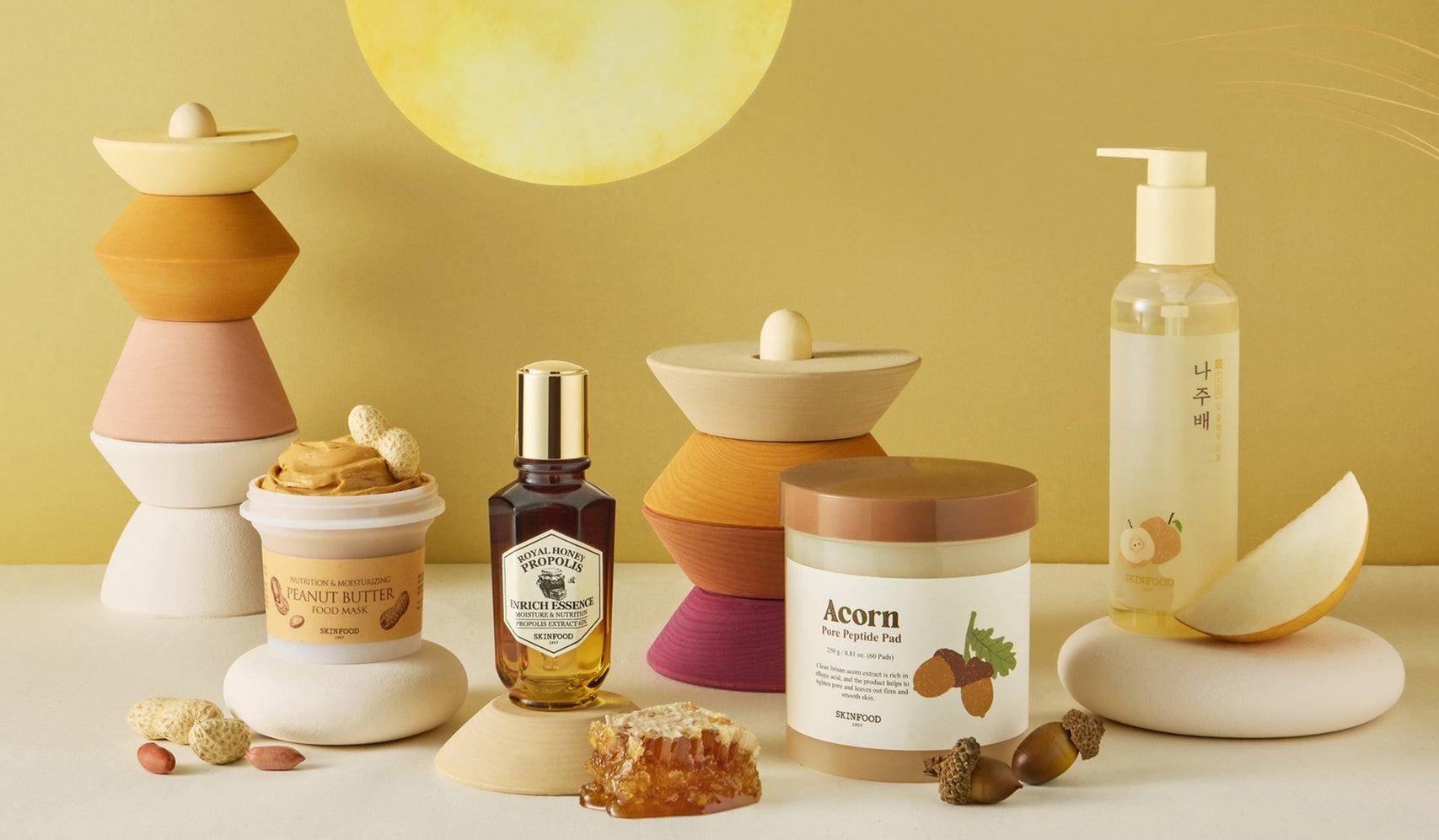 Assorted skincare products including shea butter, acorn body scrub, and facial oil on a decorative display with natural accents.
