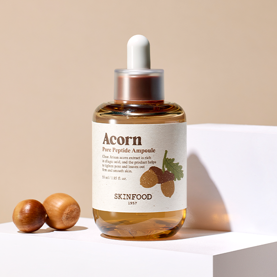 SKINFOOD Acorn Pore Peptide Ampoule 55ml on a white podium with acorns.
