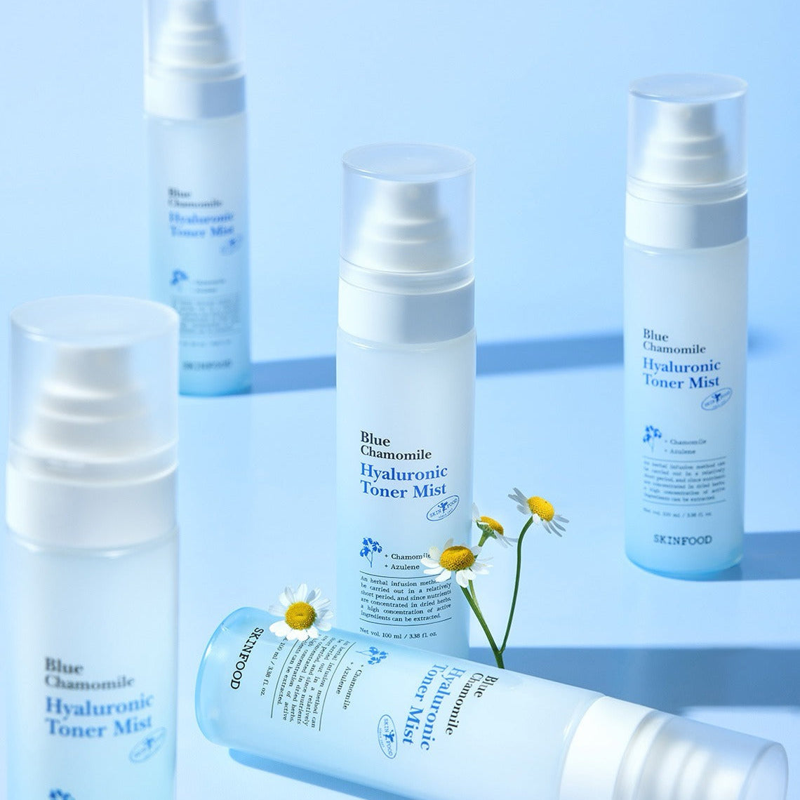 SKINFOOD Blue Chamomile Hyaluronic Toner Mist 100ml bottles arranged on a blue background with chamomile flowers.
