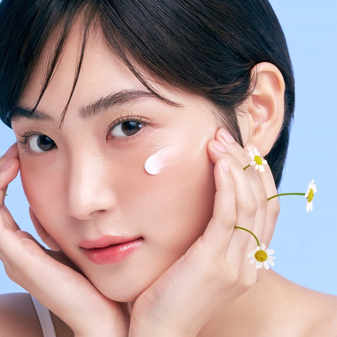 Young woman with smooth skin applying skincare cream, decorated with daisies on fingers.