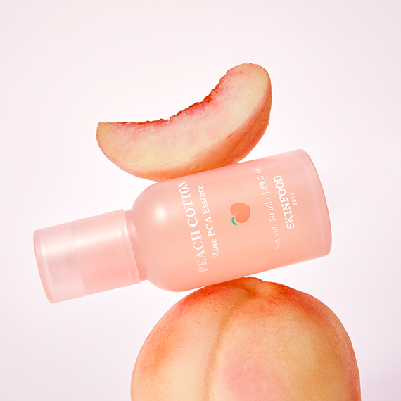 Bottle of SKINFOOD Peachy Zinc PCA Essence 50ml with a peach slice and whole peach, highlighting skincare product benefits.