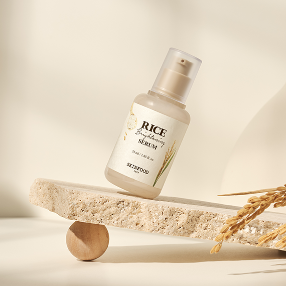 SKINFOOD Rice Brightening Serum 55ml bottle on a stone slab with decorative grasses, offering skin radiance and hydration benefits.