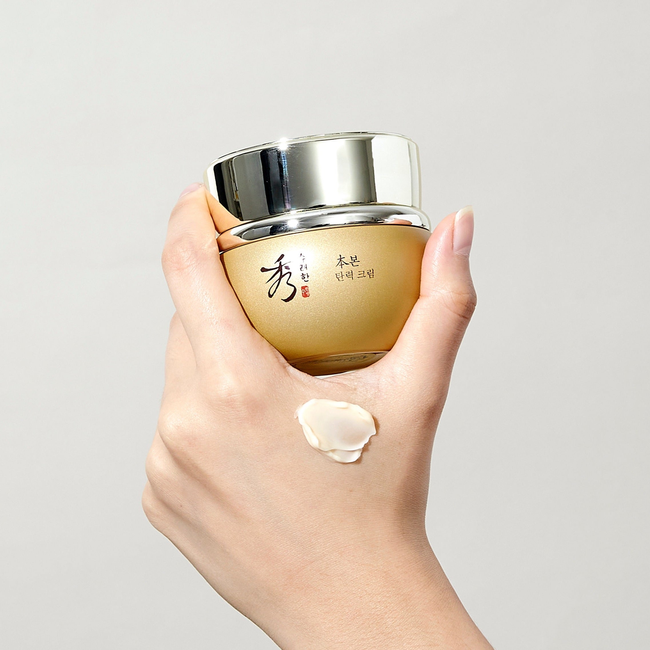 Hand holding SOORYEHAN Bon Elasticity Cream 75ml jar with swatch on skin