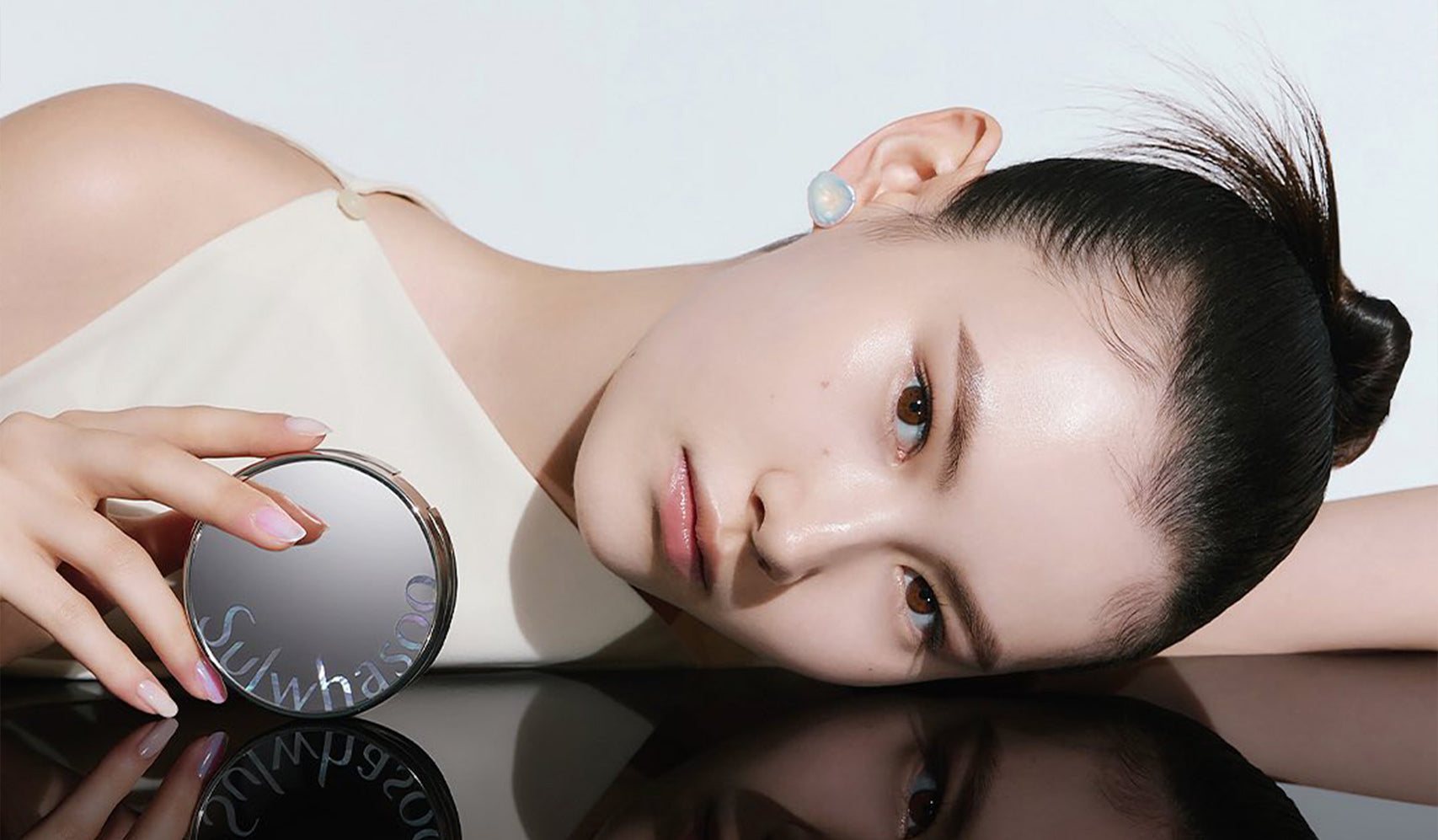 Model holding Sulwhasoo compact, showcasing radiant skin with a smooth, reflective surface.