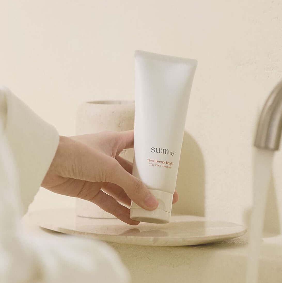 Person holding SU:M37 Time Energy Bright Clay Pack Cleanser 150ml near bathroom sink