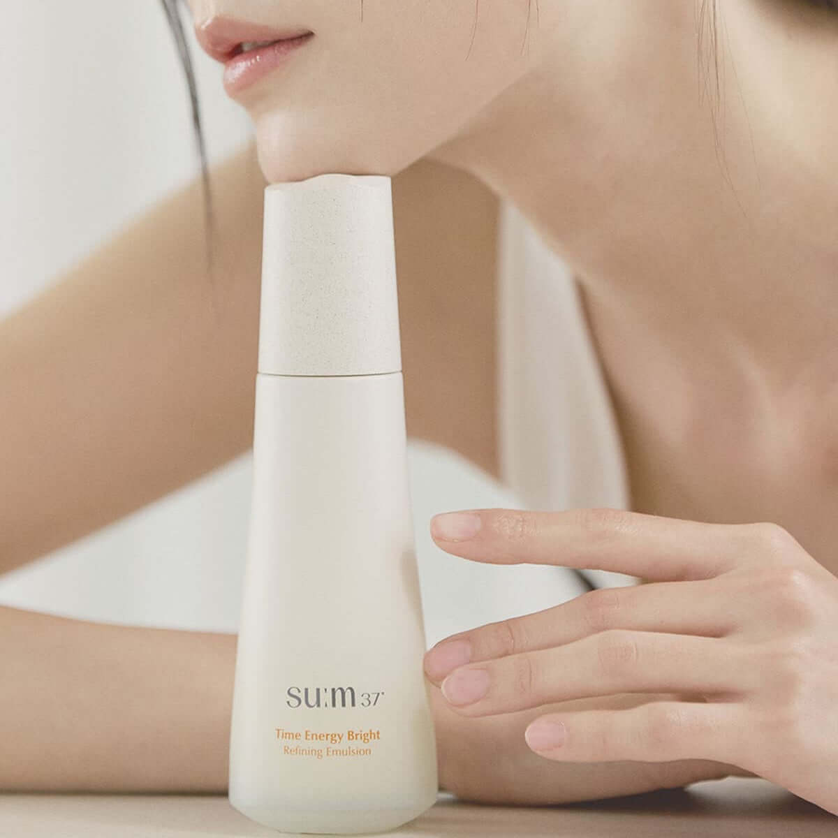 SU:M37 Time Energy Bright Refining Emulsion 120ml displayed next to a model's hand for skincare promotion.