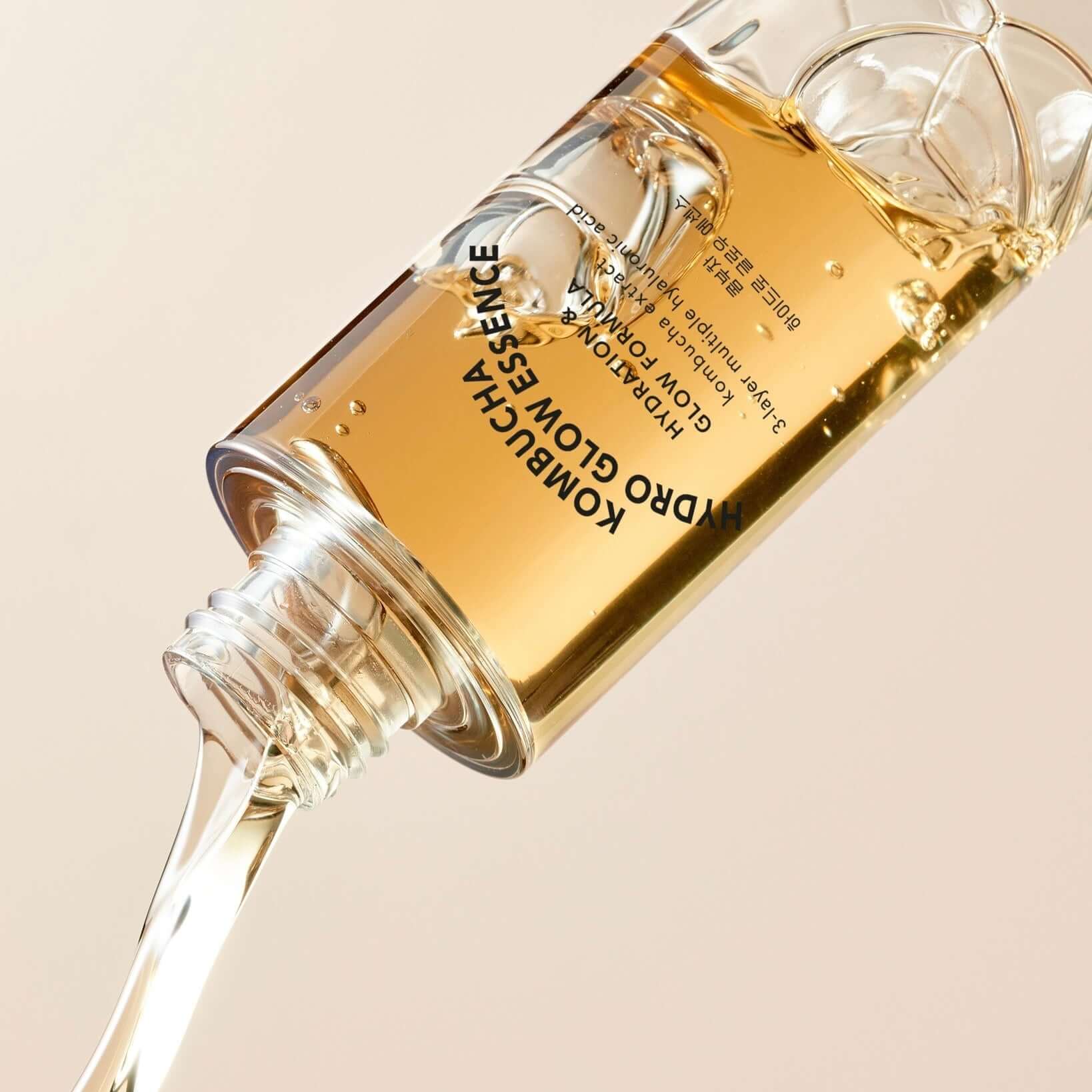 T'ELSE Kombucha Hydro Glow Essence 150ml bottle with liquid pouring out, skincare product in focus on beige background.