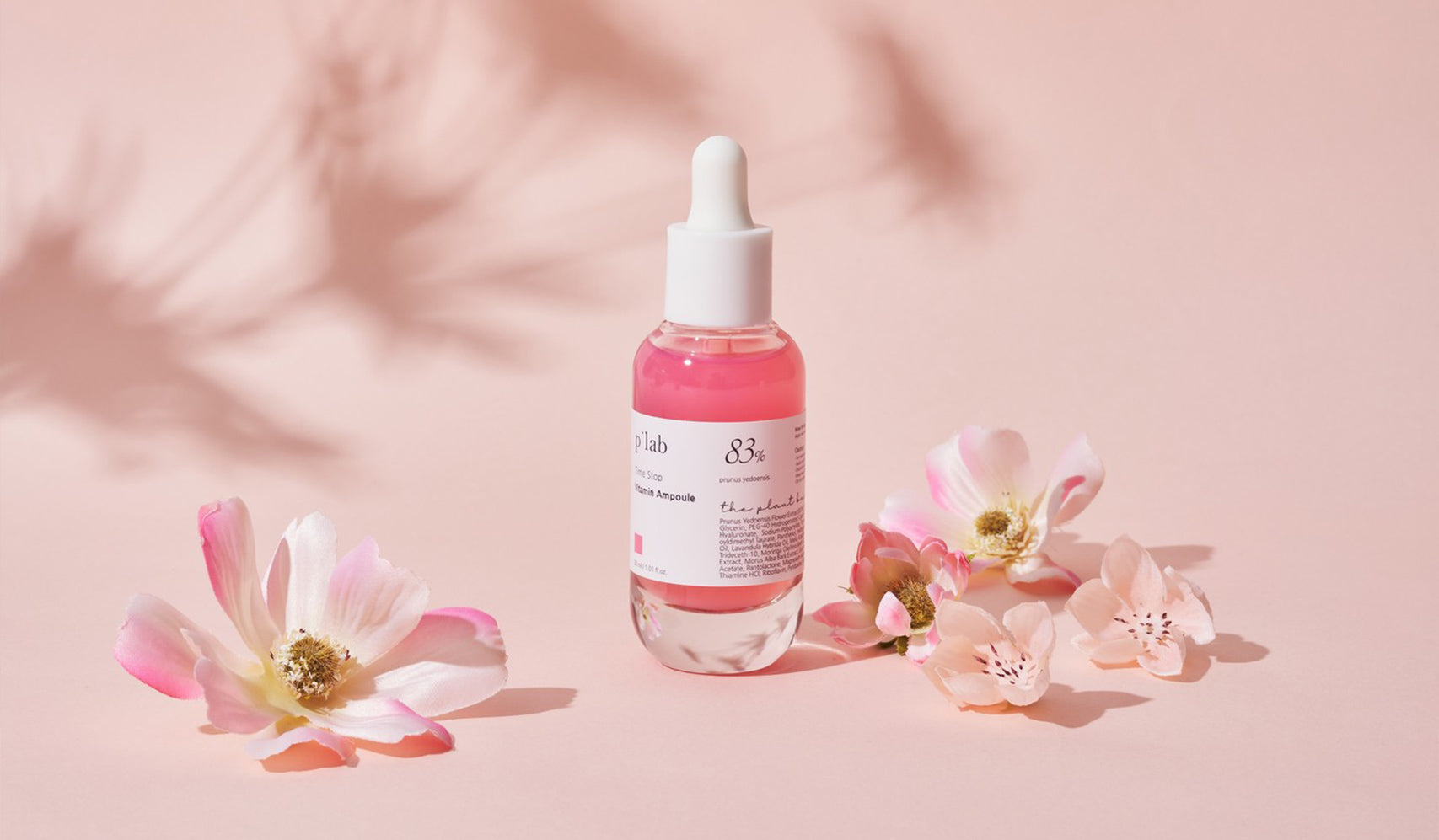 Pink serum bottle with dropper surrounded by cherry blossom flowers on a soft pink background, creating a delicate skincare aesthetic.