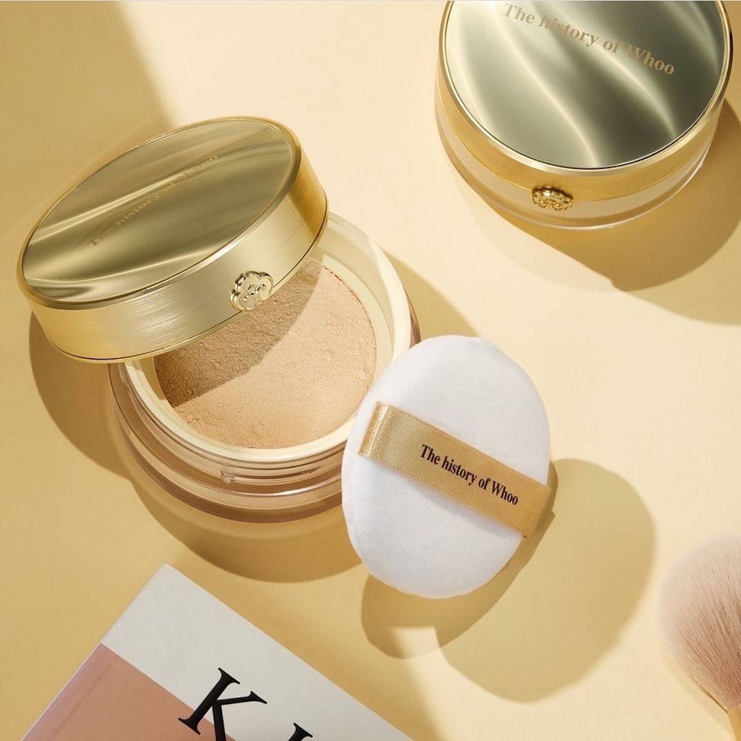 THE WHOO Gong Jin Hyang Mi Luxury Luminous Powder with puff on table, elegant packaging in gold with branding details.