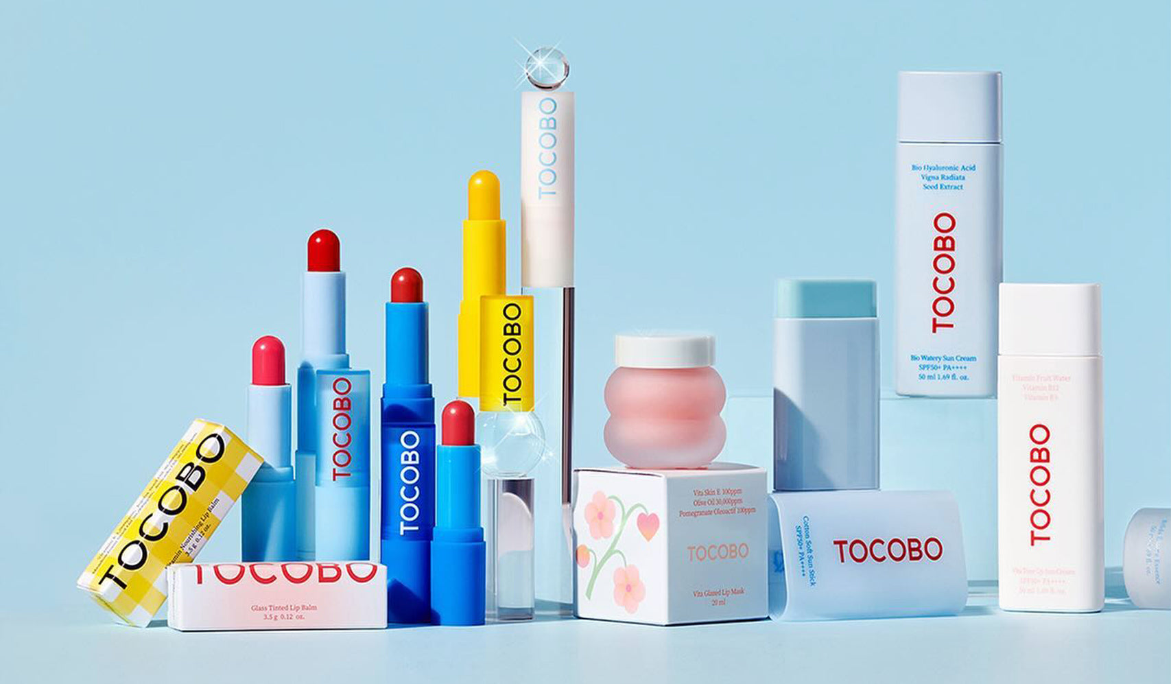 Assorted Tocobo cosmetics displayed on a blue background, including lipsticks, creams, and boxes.