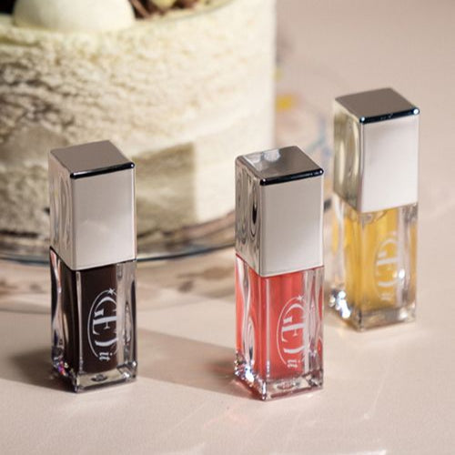 Three bottles of TONY MOLY Get It Lip Oil in different shades, displayed on a table with a blurred background.