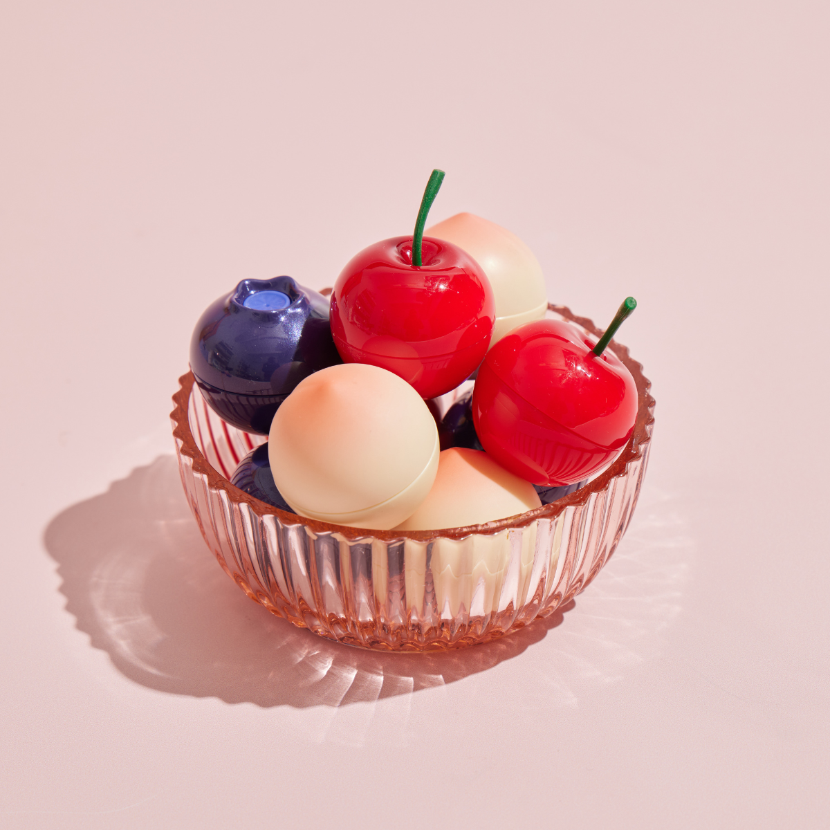 TONY MOLY MIN Fruit Lip Balm in a glass bowl, showcasing colorful fruit-themed packaging on a soft pink background.