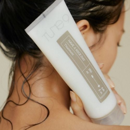 Woman holding TONYMOLY Tune 9 Have A Nice Day Treatment 250ml bottle near her face, showcasing product packaging and design.