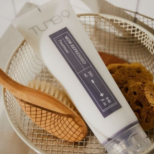 Tube of TONYMOLY Tune 9 Wow Refreshing Treatment 250ml on a basket with brushes and sponge, showcasing hair care product.