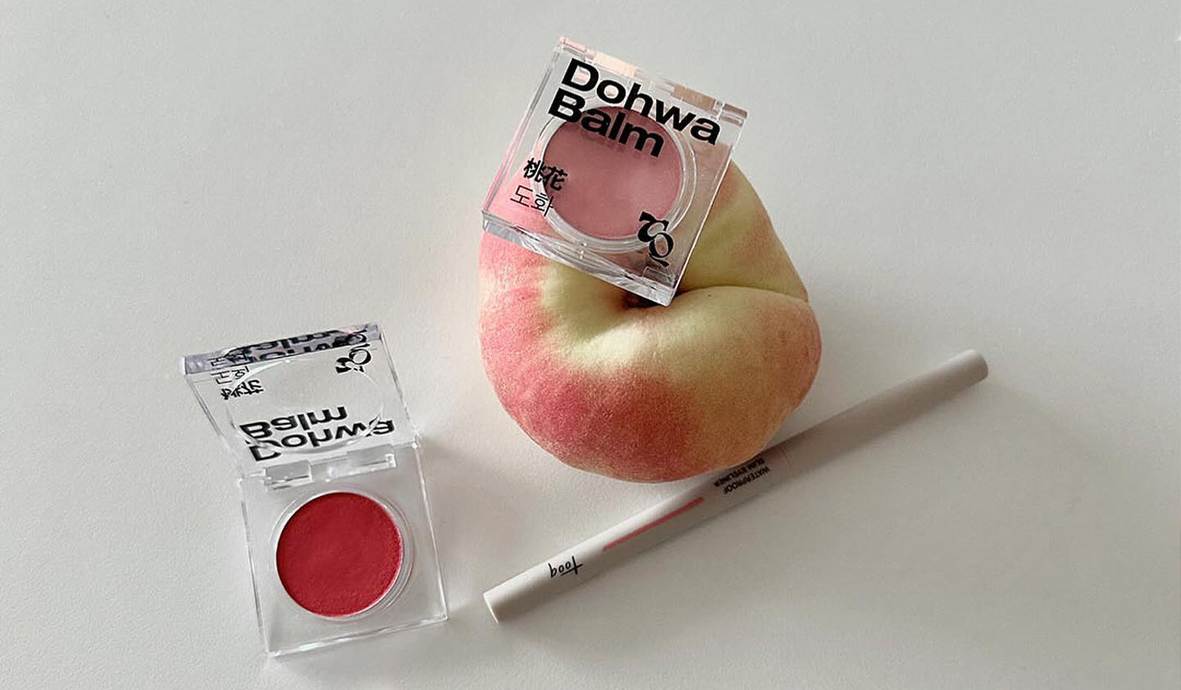 Dohwa Balm and makeup products with peach on white background.