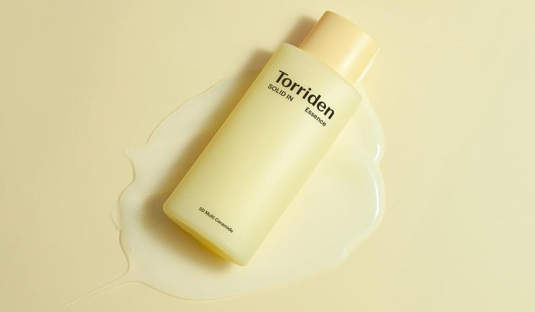 Torriden SOLID IN Essence bottle on a beige background with liquid spillage, showcasing skin care packaging and texture.