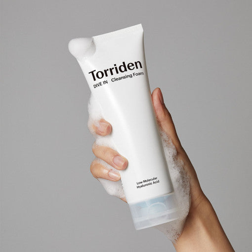 Hand holding a tube of TORRIDEN Dive In Low Molecular Hyaluronic Acid Cleansing Foam 150ml with foam lather