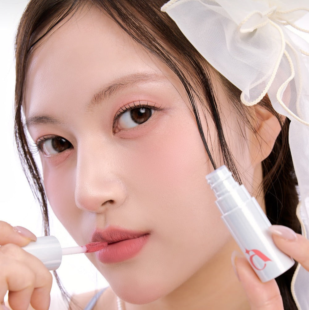 Woman applying UNLEASHIA Clound Kiss Velvet Tint on her lips, showcasing soft pink color and smooth velvet finish.