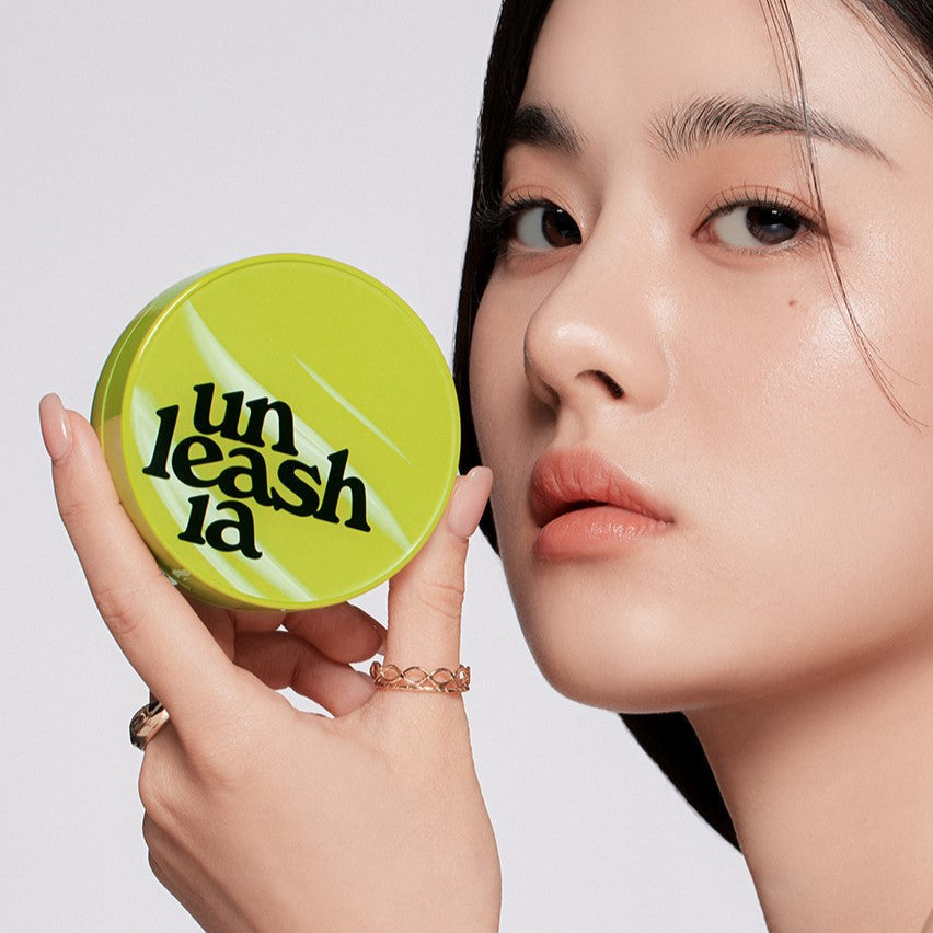 A woman holding a UNLEASHIA Satin Wear Healthy Green Cushion compact, highlighting the product's sleek design and vibrant green color.