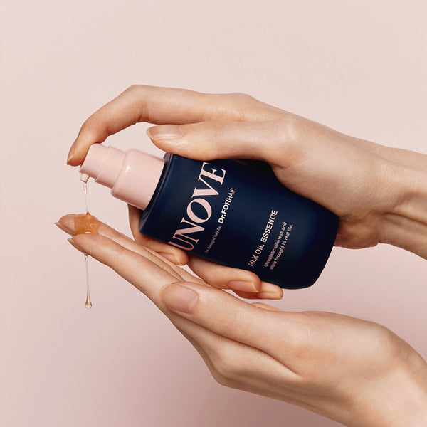 Hands dispensing UNOVE Silk Oil Essence 70ml from blue bottle on light background