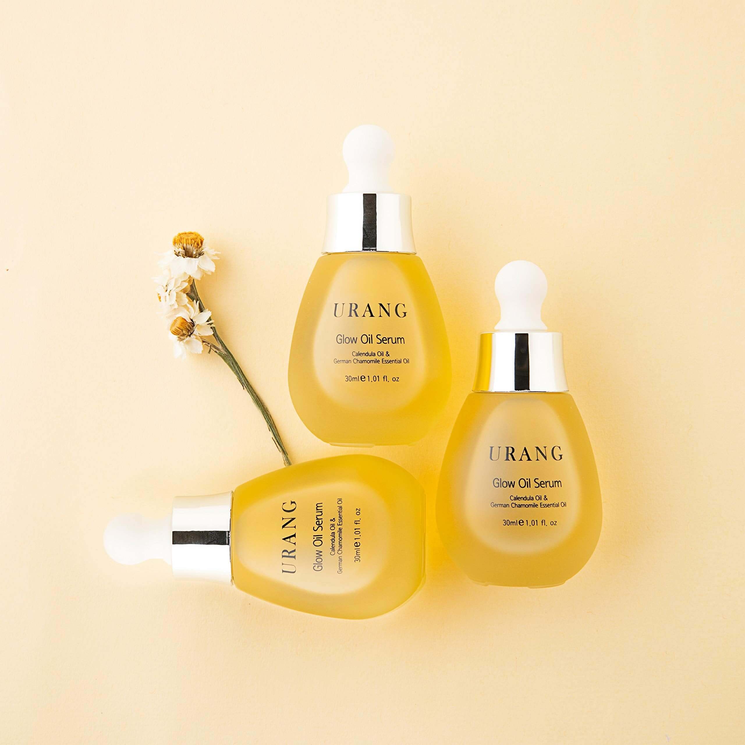 URANG Glow Oil Serum 30ml bottles displayed on a soft yellow background with floral accents