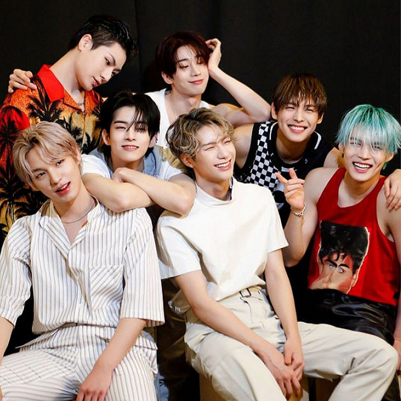 Seven young men posing together in a vibrant and joyful manner against a dark background, wearing fashionable casual attire.