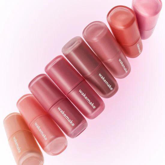 Assorted shades of WAKE MAKE Water Blurring Layer Tint 4.6g tubes on a pink background.