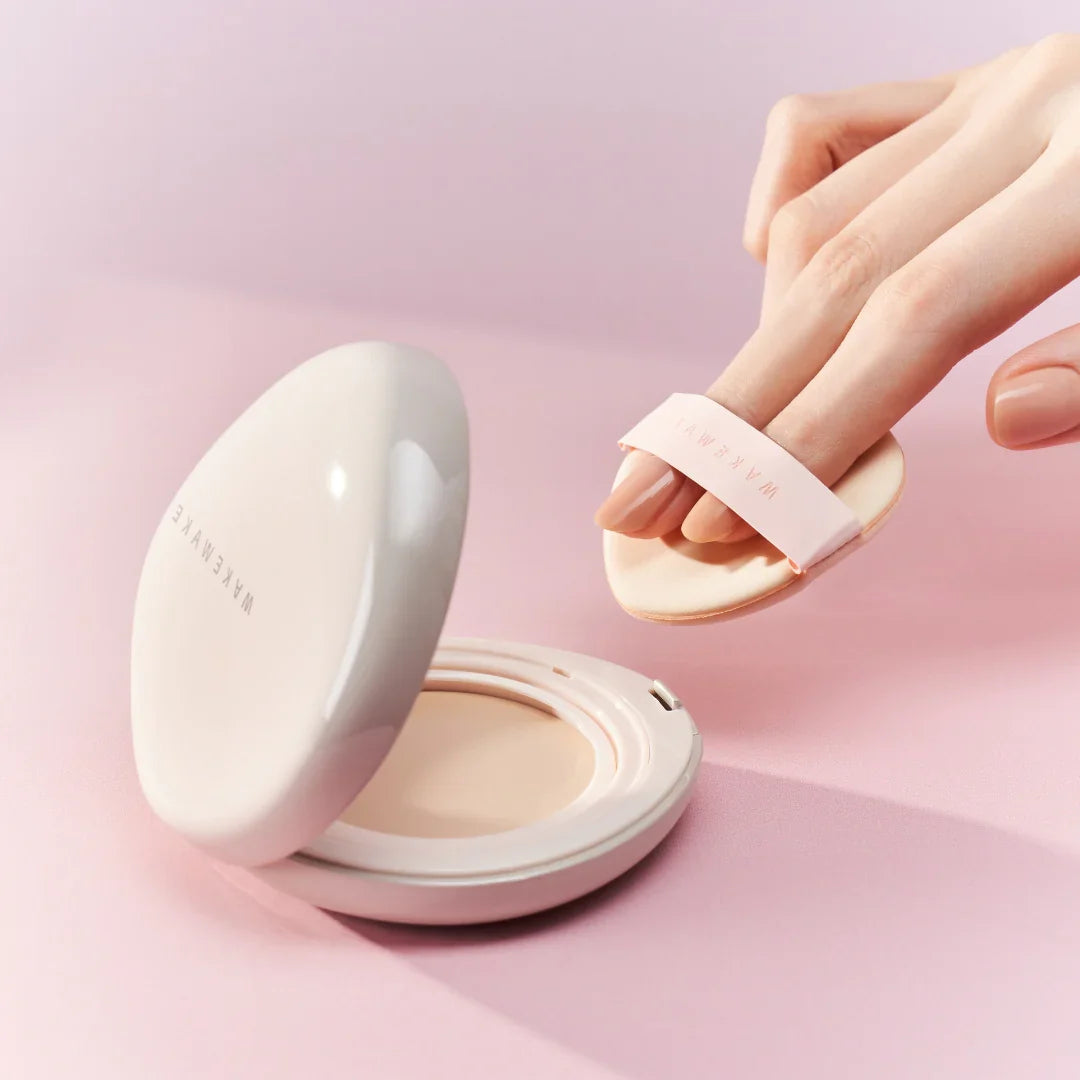 Person applying WAKE MAKE Water Glow Coating Balm 12.5g with a makeup applicator on a pink background