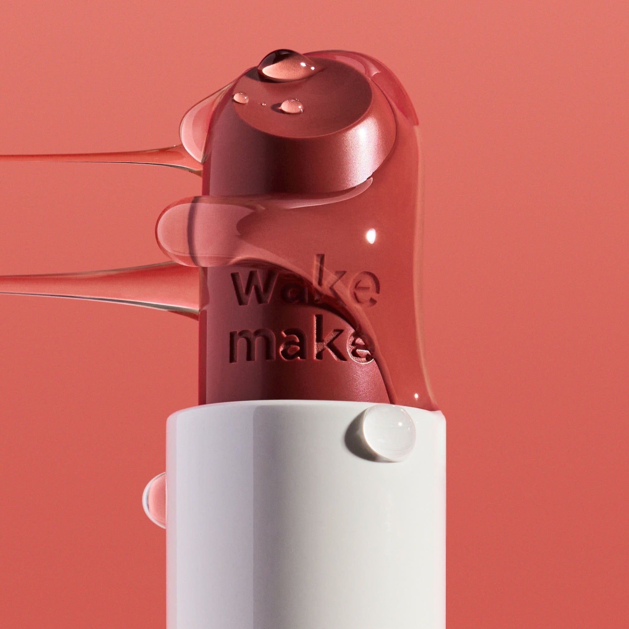 WAKEMAKE Healthy Glow Balm Sticks in a sleek tube with glossy pink balm on a coral background