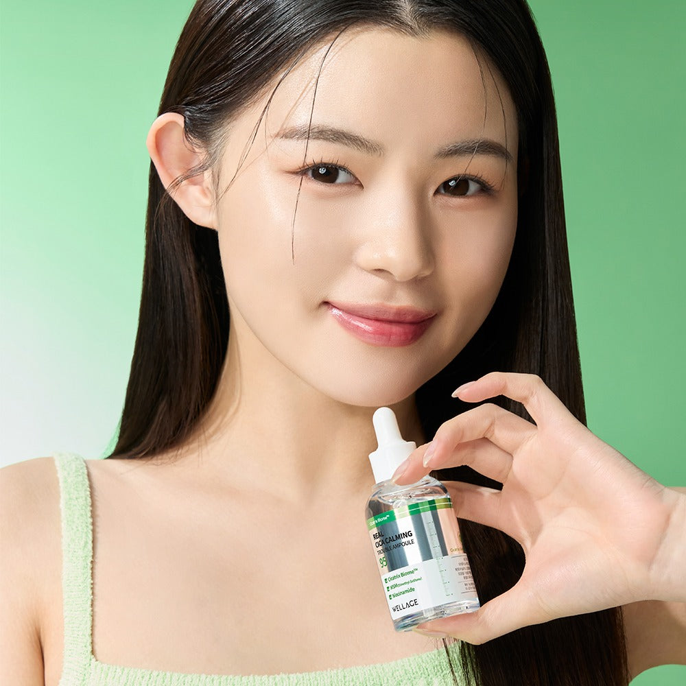 WELLAGE Real Cica Calming 95 Trouble Ampoule 50ml held by a smiling model against a green background for skincare promotion.