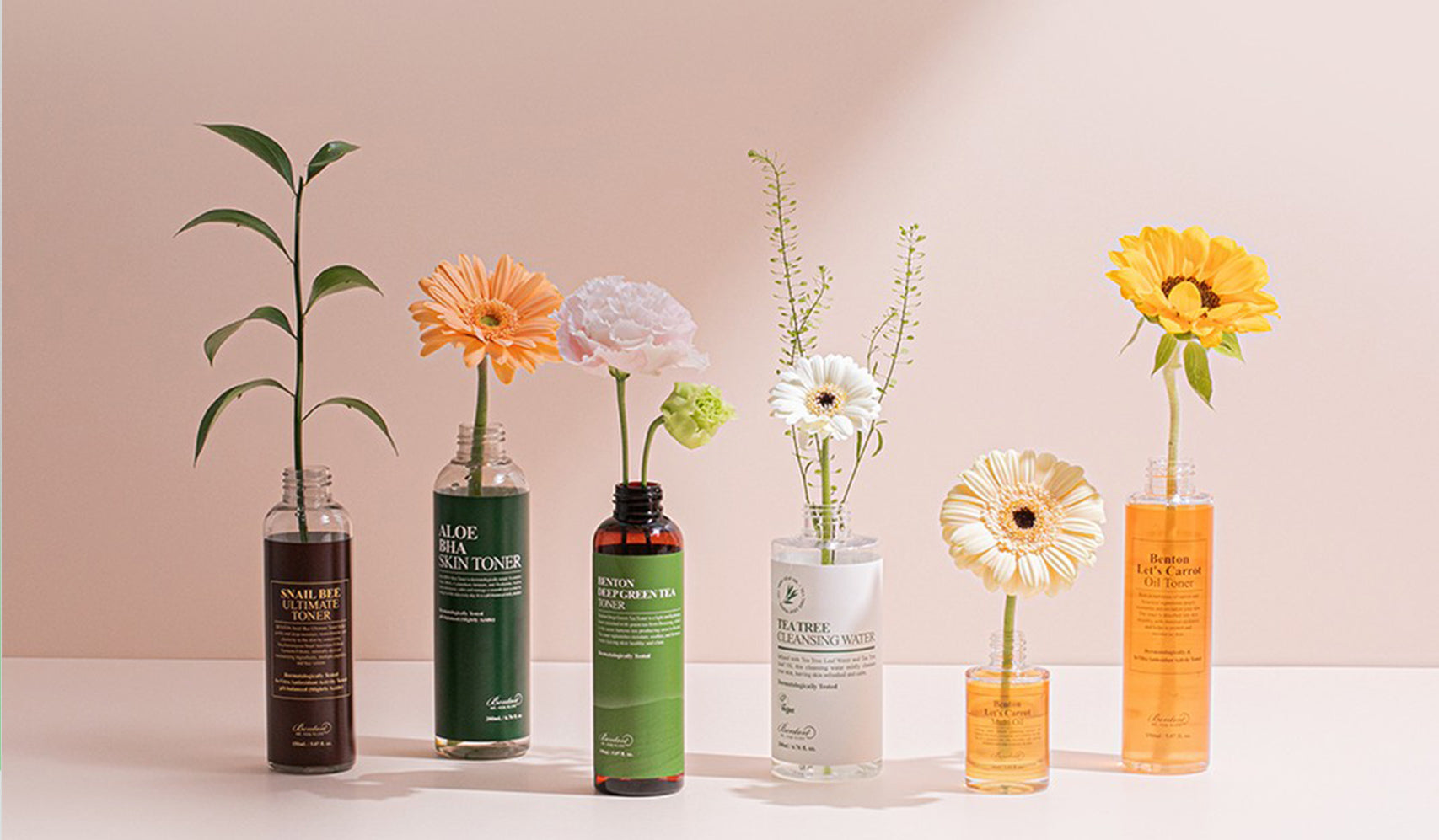 Assorted skincare bottles with flowers on a pink background