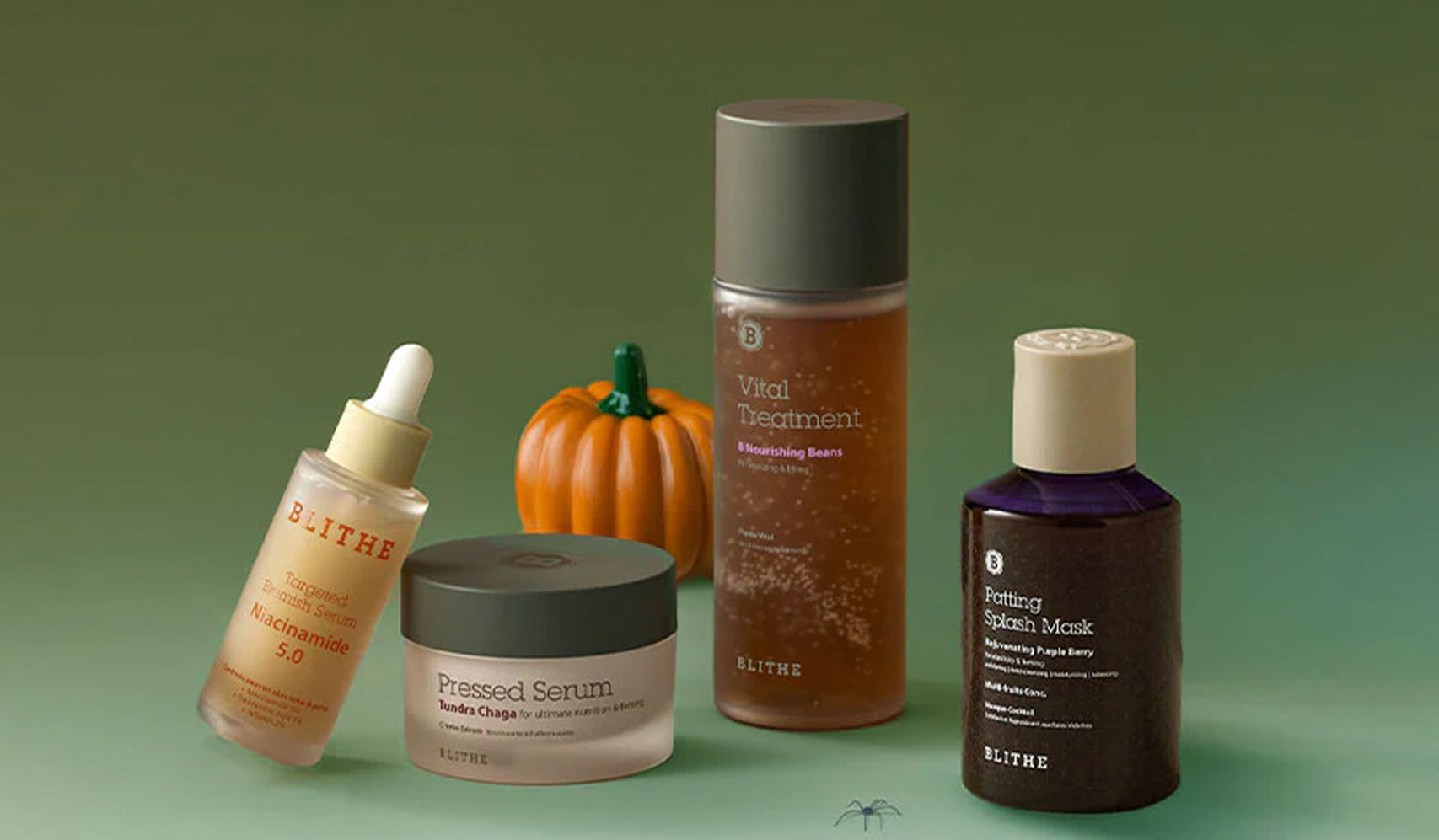 Blithe skincare products displayed on a green surface with a small pumpkin for an autumn-themed presentation.