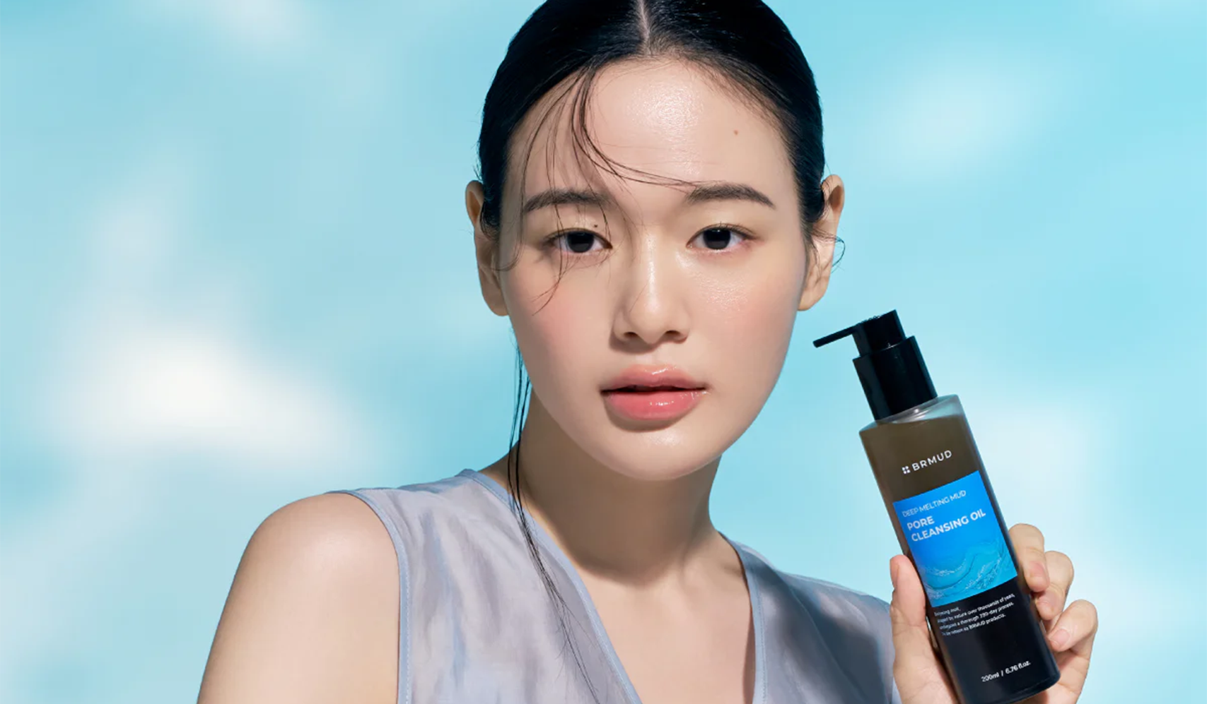 Person holding a bottle of Iunik Calendula Complete Cleansing Oil against a blue sky background.