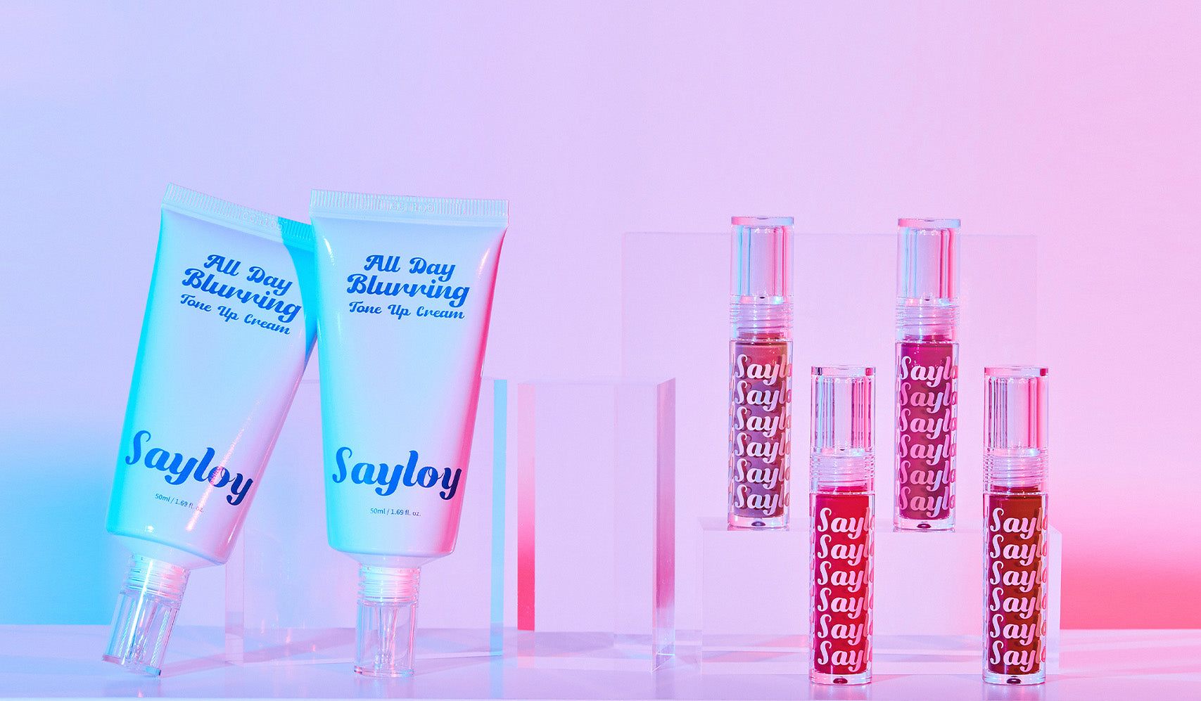 Sayloy beauty products including All Day Blurring tone-up creams and lip tints on display with vibrant pink and blue lighting.