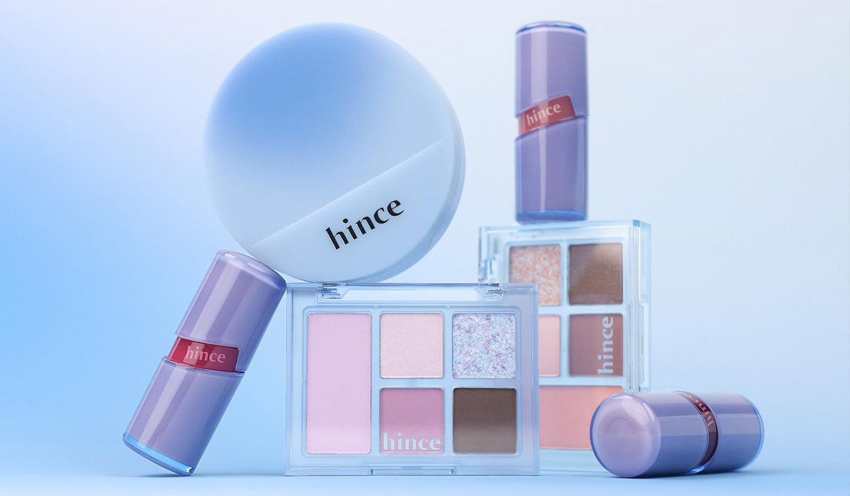 Collection of hince makeup products featuring compact powders and lipsticks in pastel shades on a blue background.