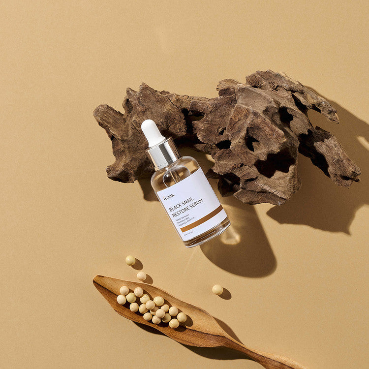 iUNIK Black Snail Restore Serum 50ml on wooden background with decorative elements; skincare product for hydration and repair.
