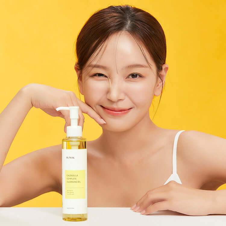 Woman holding iUNIK Calendula Complete Cleansing Oil 200ml against yellow background.