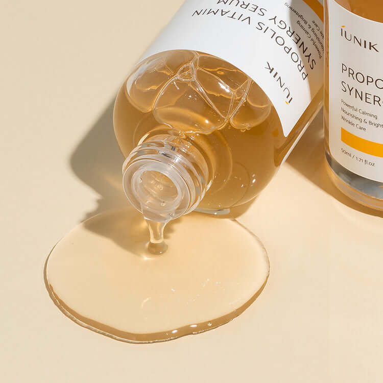 iUNIK Propolis Vitamin Synergy Serum 50ml bottle with spilled serum on a beige surface.