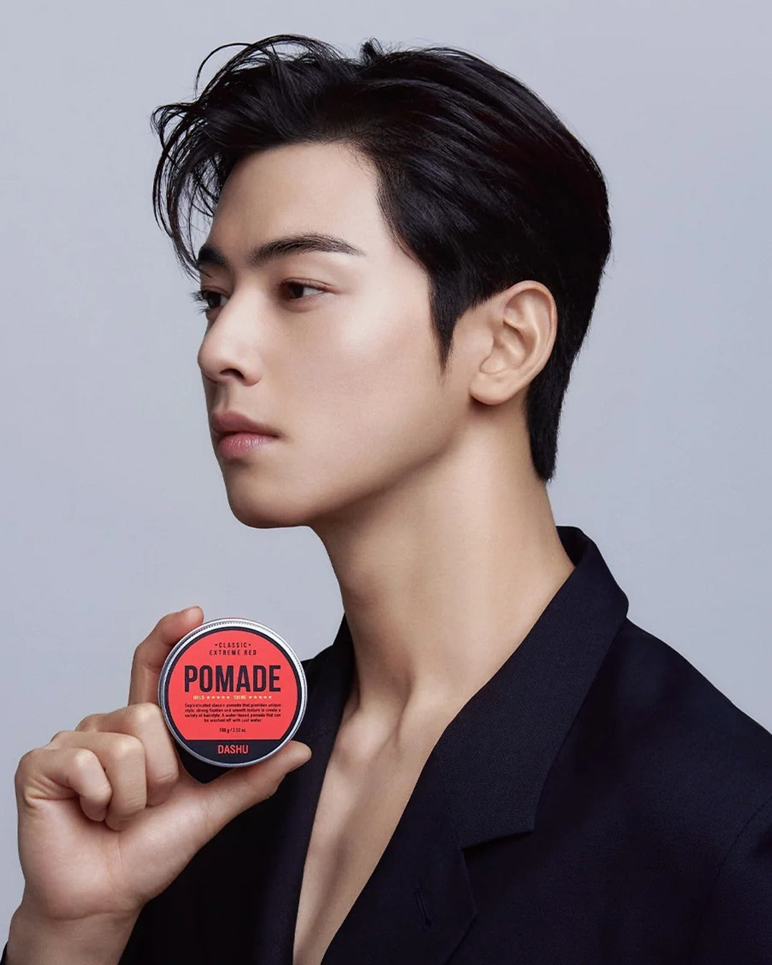 Person holding a can of hair styling pomade with sleek, styled hair.