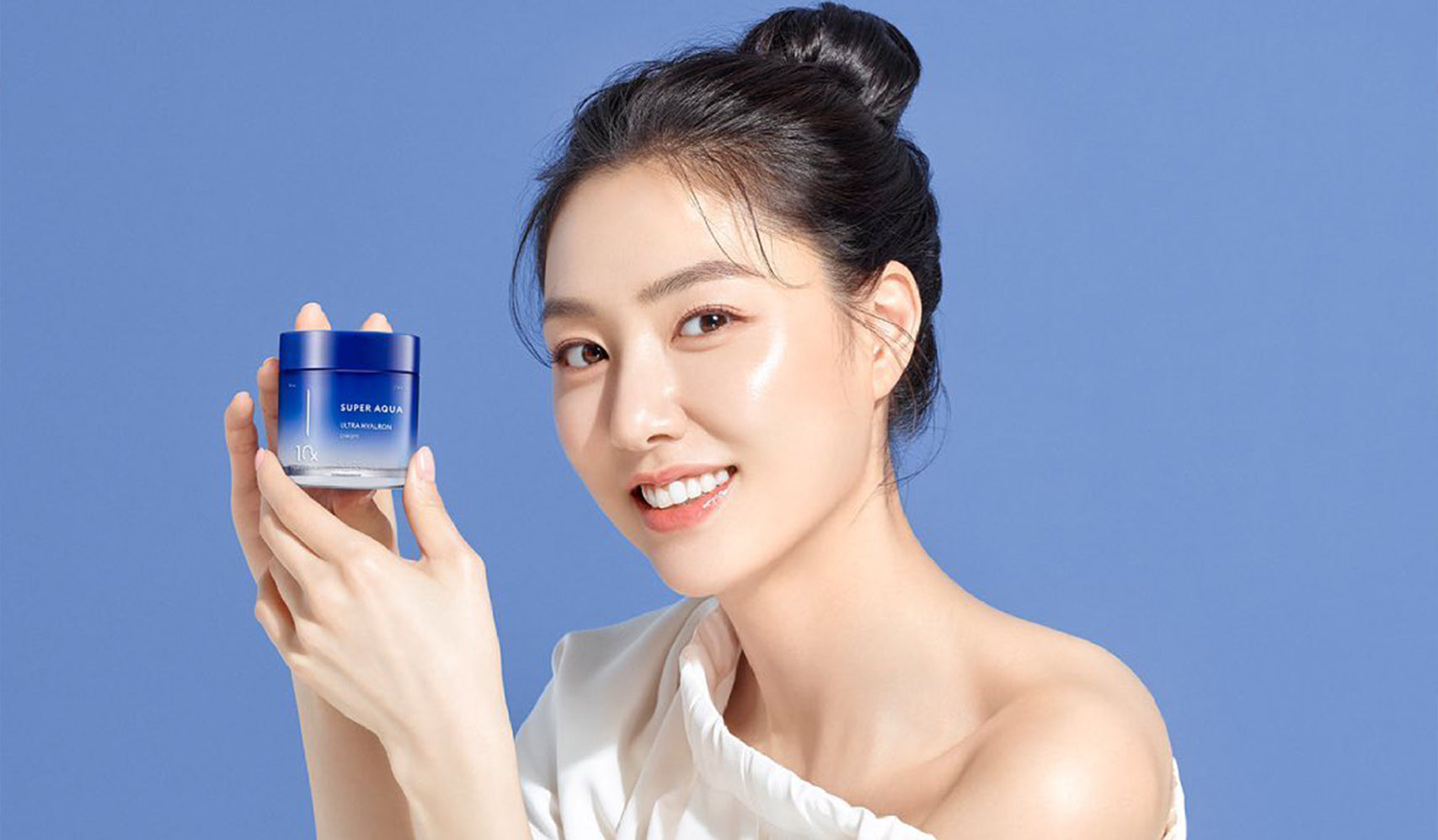 Smiling woman holding a blue skincare jar against a blue background