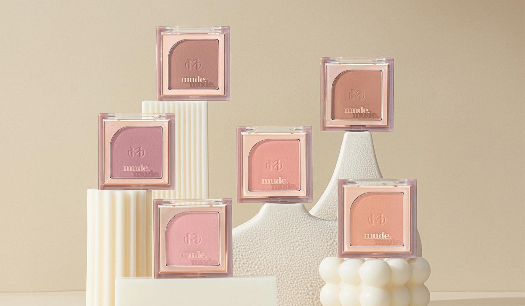 Assorted makeup blush palettes displayed on geometric shapes against a neutral background