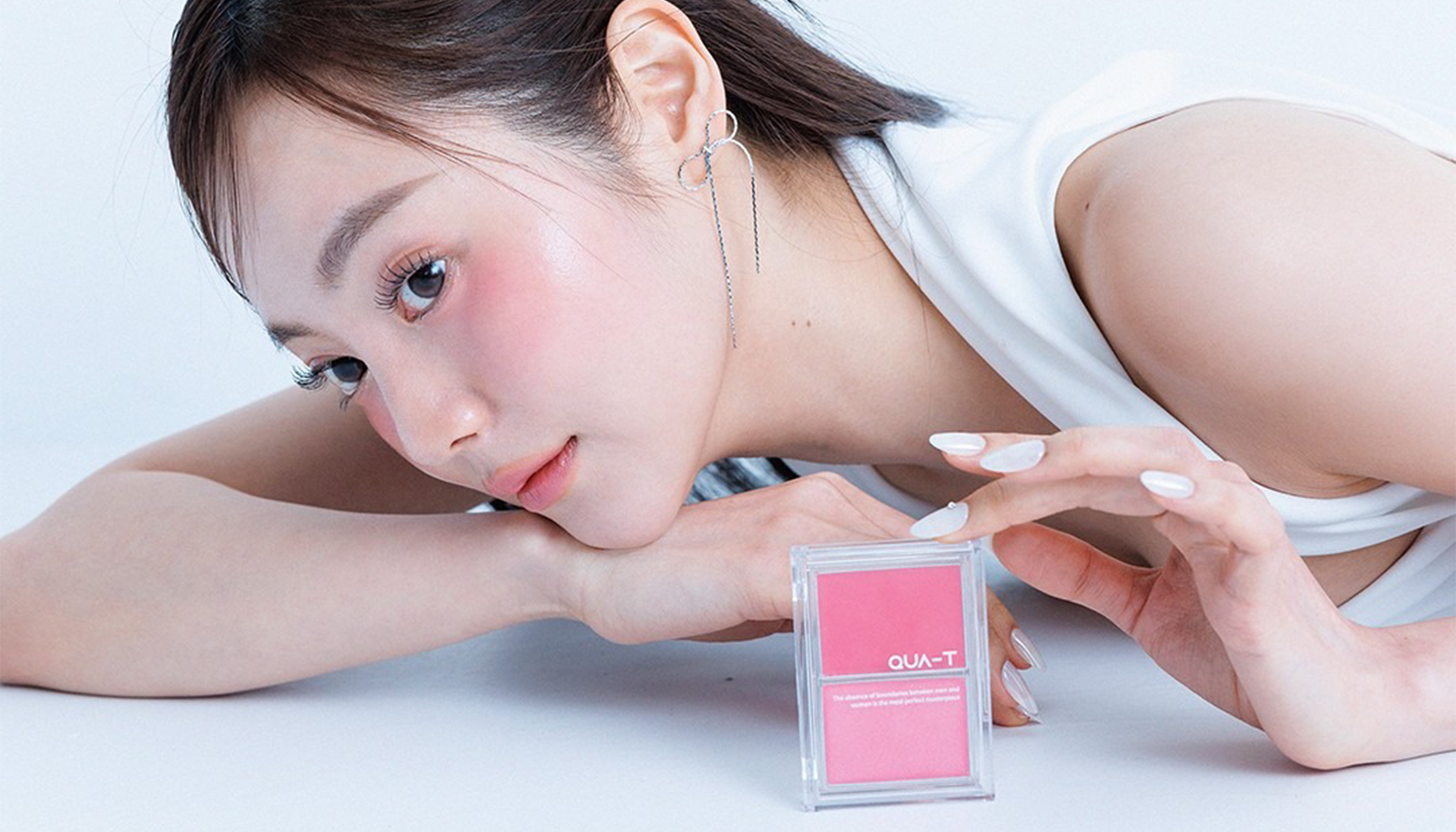 Woman posing with pink QUAT-T makeup compact on a white background.