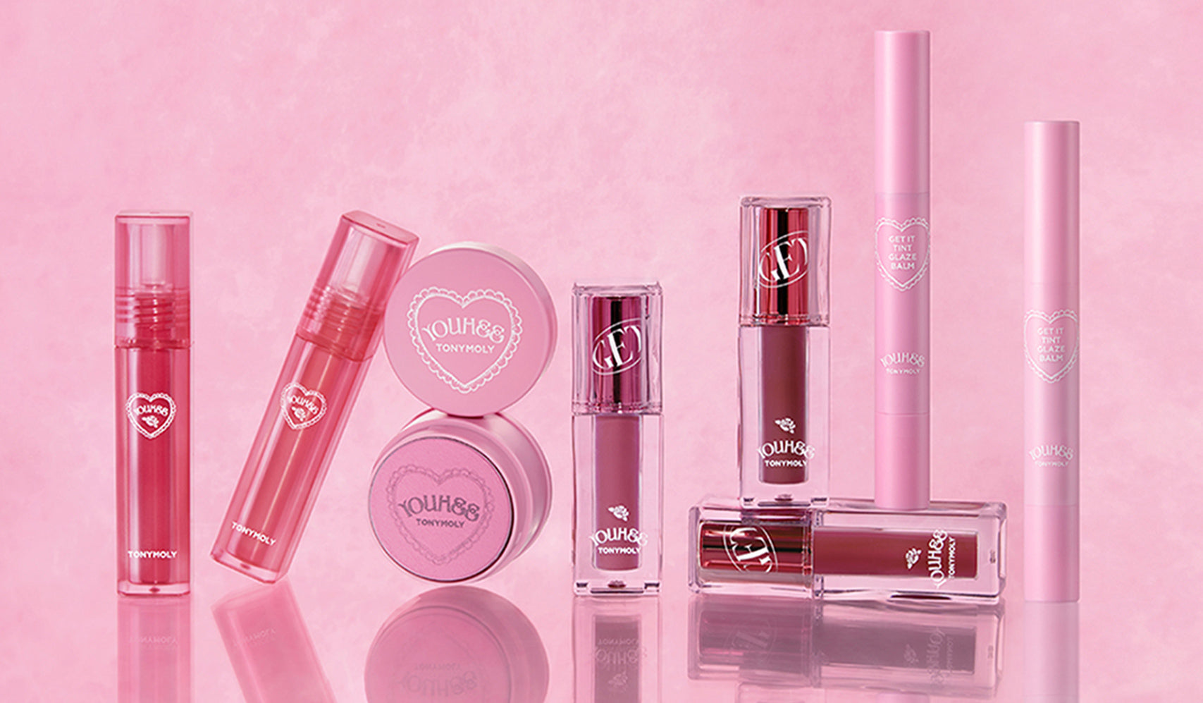 Collection of pink and red makeup products in sleek packaging against a soft pink background.